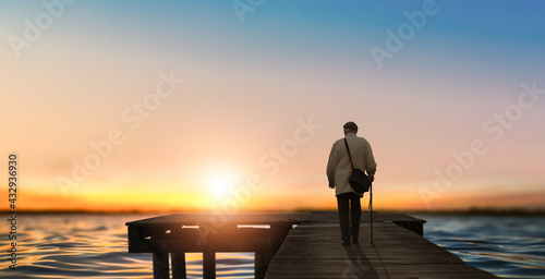 Old man watches the morning sea over pier sunset.