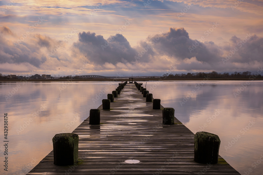 Naklejka premium Storm clouds in the distance over a wooden pier, reflecting in the water. Island Beach State Park New Jersey