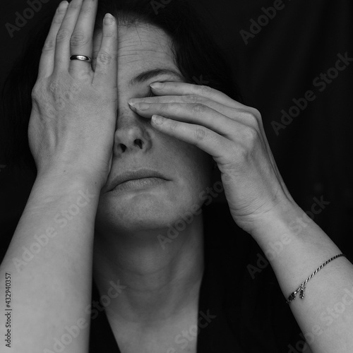 Portrait of a woman rubbing her eyes. Black and white portrait with hands. Emotional portrayal of a person. 
