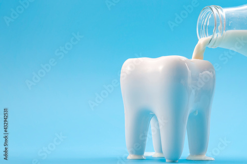 Oral health, cavity prevention and calcium rich drink for strong teeth concept with glass bottle pouring milk into a heathy tooth isolated on blue background with copy space