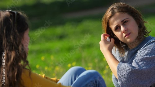 young woman sitting on the meadow at park confides in a friend