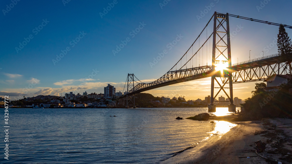 Obraz premium Pôr do sol e raios solares ultrapassando a estrutura da Ponte Hercílio Luz , Santa Catarina, Brasil, florianopolis , Florianópolis