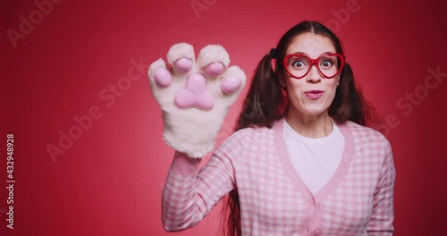 Friendly funny girl in a heart shaped glasses and cute waves her hand and says hello in front of the camera on red background. Cute welcome hello concept