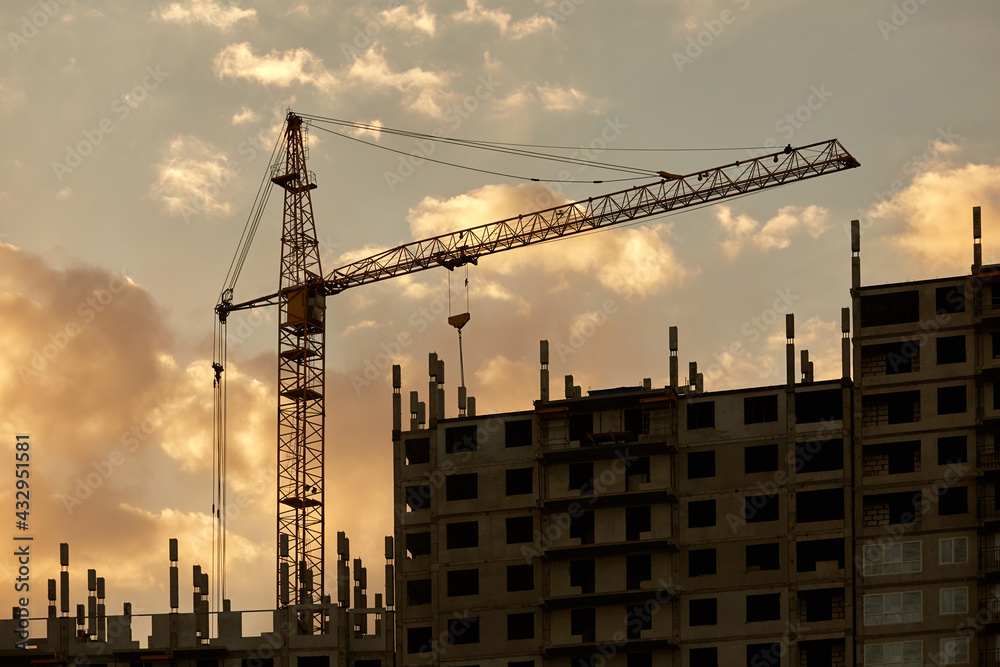 The silhouette of a building under construction. Sunset silhouettes of high-rise buildings under construction with cranes against the sky with clouds and the setting sun The silhouette of a building under construction. Sunset silhouettes of high-rise buildings under construction with cranes against the sky with clouds and the setting sun