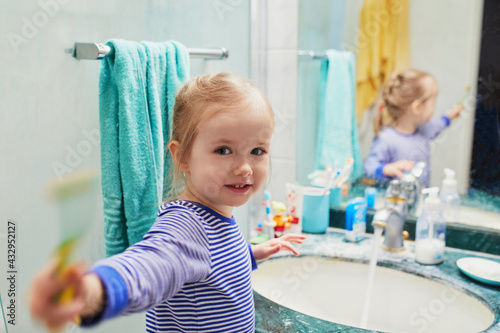Happy toddler girl in pyjamas brushing her teeth in bathroom
