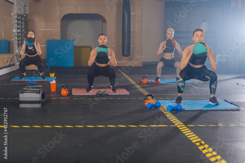 Fitness group of four attractive women doing exercises and squats with a medicine ball
