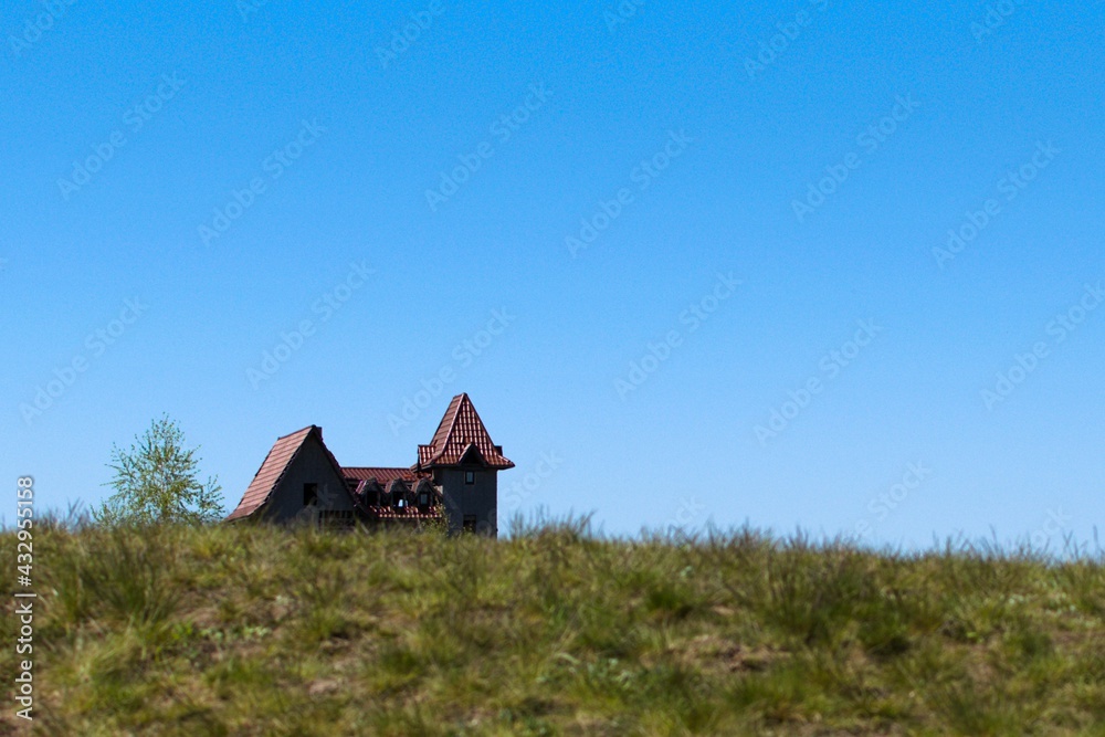 House with tiled roof and turrets against blue sky. Blurred foreground with green grass