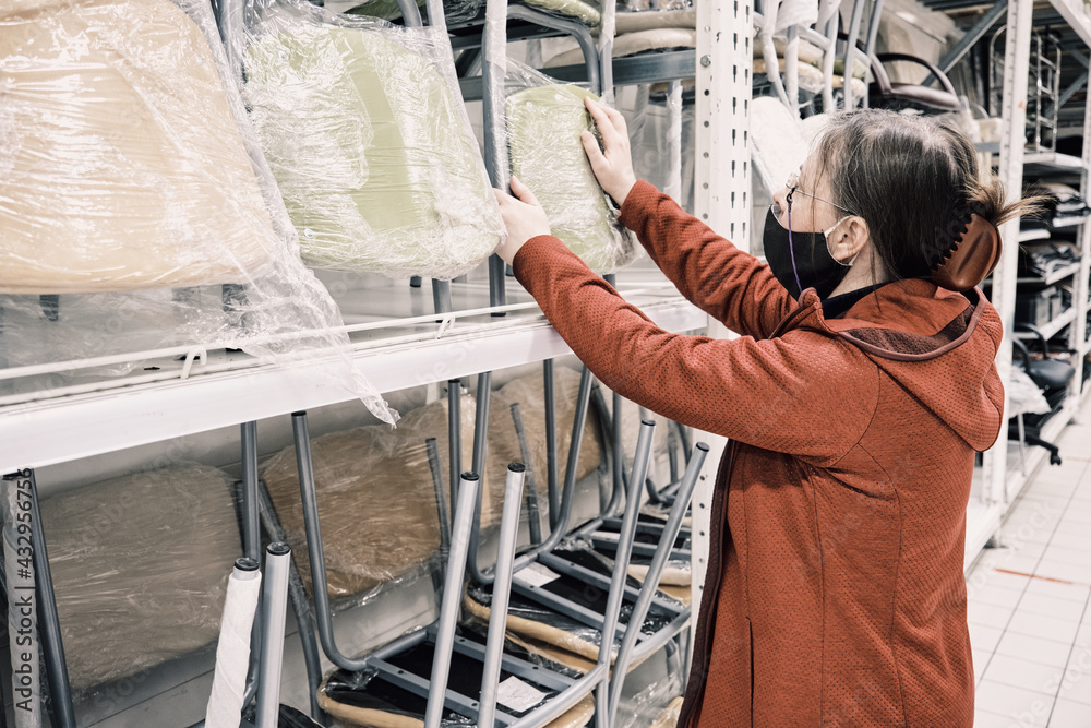 Woman in a mask against the virus chooses a new light green chair in the store to buy. Concept of buying new furniture for home and office Woman in a mask against the virus chooses a new light green chair in the store to buy. Concept of buying new furniture for home and office