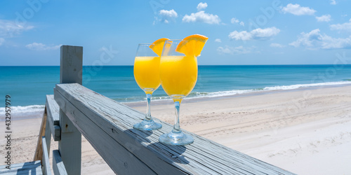 Two glasses brightly lit by the sun with a mimosa cocktail against the background of the blue sea as a symbol of comfortable relaxation