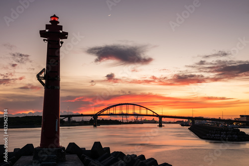 Amazing sunset in the city of Ishigaki with its silhouetted bridge, colorful sky with a waxing crescent, a signal light for navigation lit in the foreground. photo