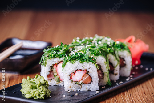 Sushi on a wooden table in restaurant. Portion of sushi served on black plate with wasabi, soy sauce, ginger and chopsticks. Delicious Japanese food. Sliced tasty sushi rolls, close-up