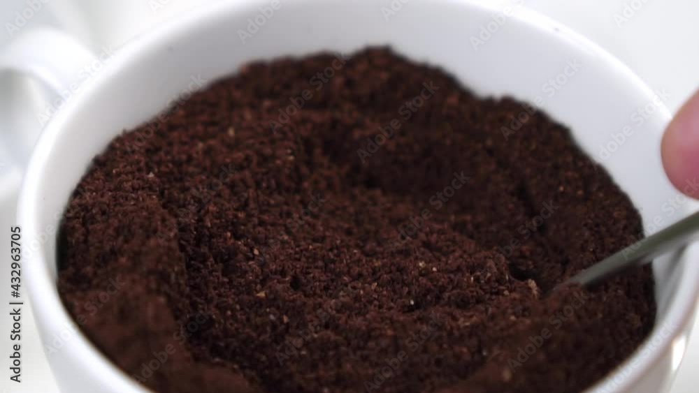 Ground milled uncooked coffee blend in a white cup. Mixing with a teaspoon in slow motion. Macro shot. Aromatic traditional energy natural drink Ground milled uncooked coffee blend in a white cup. Mixing with a teaspoon in slow motion. Macro shot. Aromatic traditional energy natural drink