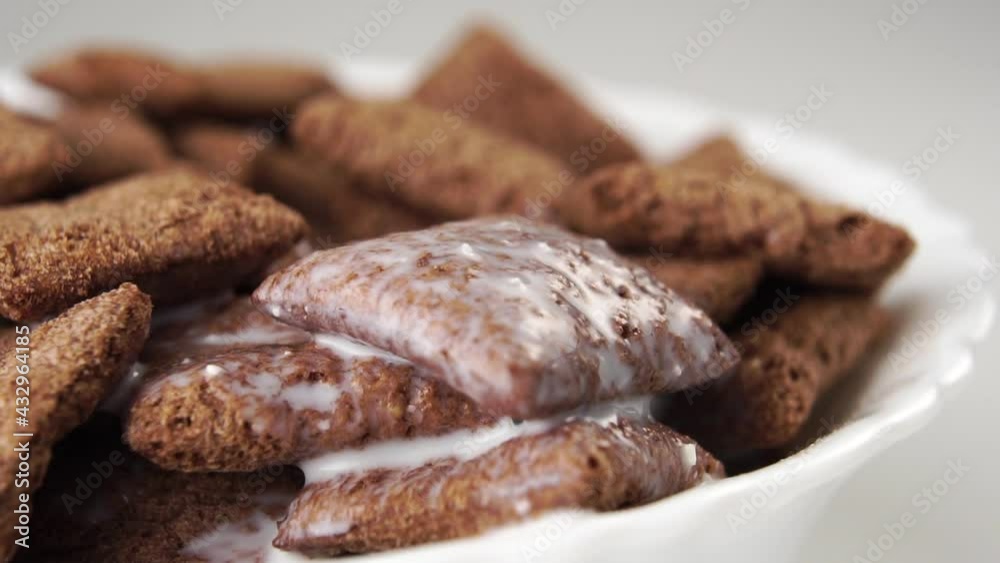 Milk is soaked in a chocolate cereal pad of cereal in a full white bowl of nutritious breakfast. Porous dry surface. Macro shot. Slow motion Milk is soaked in a chocolate cereal pad of cereal in a full white bowl of nutritious breakfast. Porous dry surface. Macro shot. Slow motion