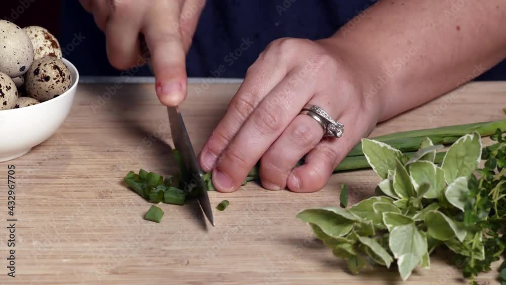 Close up of knife chopping or dicing fresh green onions on wooden cutting board Close up of knife chopping or dicing fresh green onions on wooden cutting board