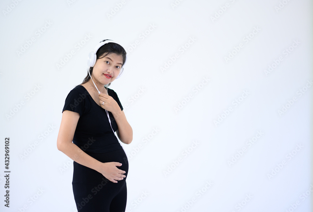 Pregnant woman wearing headphones wearing a black dress standing on a white background Pregnant woman wearing headphones wearing a black dress standing on a white background