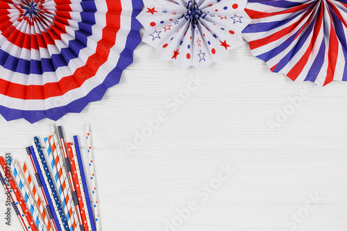 Decorations for 4th of July day of American independence, flag, straws, paper fans. USA holiday decorations on a white wooden background, top view, flat lay 