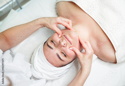 Young woman lying with closed eyes and having face and head massage. Beautiful girl has a facial massage in a beauty clinic. Cosmetologist doing massage for woman. Facial massage beauty treatment. © elenbessonova