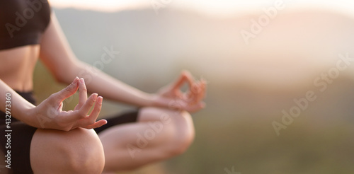 Close up with selective focus of hands woman sitting in yoga lotus pose outdoor at sunrise, meditating for balance. Horizontal banner view for website header design with copy space for text. 