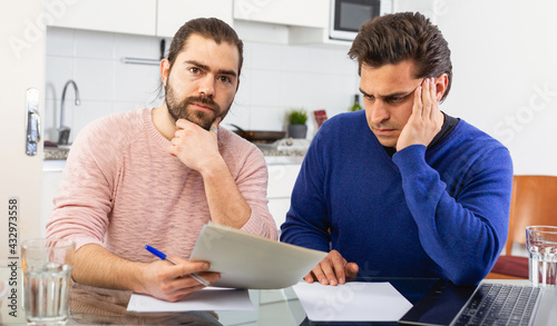 Man having problems with some documents, worriedly discussing with friend at home table. High quality photo