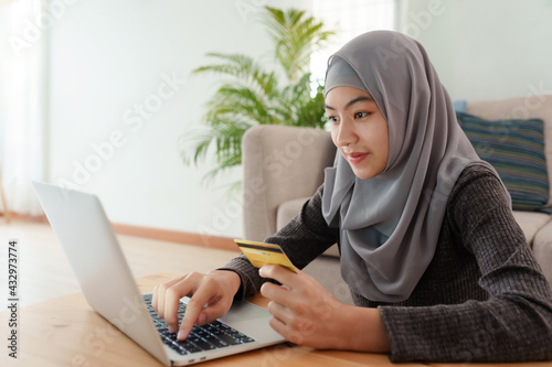 Muslim women wear hijab are buying online with a credit card on laptop and doing online transactions at home