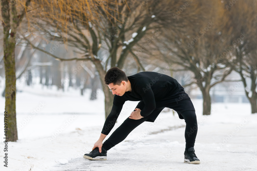 Young man doing makes stretching in morning exercises, doing fitness outdoors in winter.