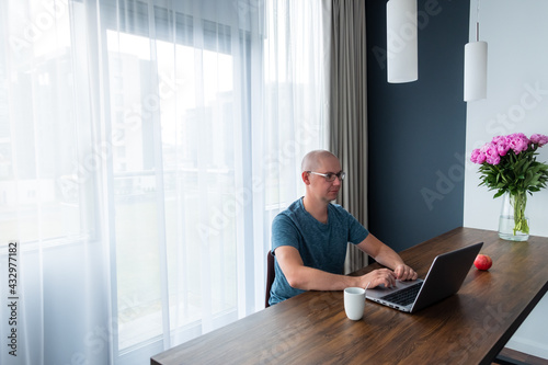 Man in a blue t-shirt sitting at the table and using laptop. Remote work, work from home.