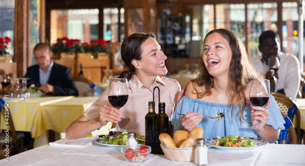 Two positive females dining in restaurant, enjoying meal and conversation