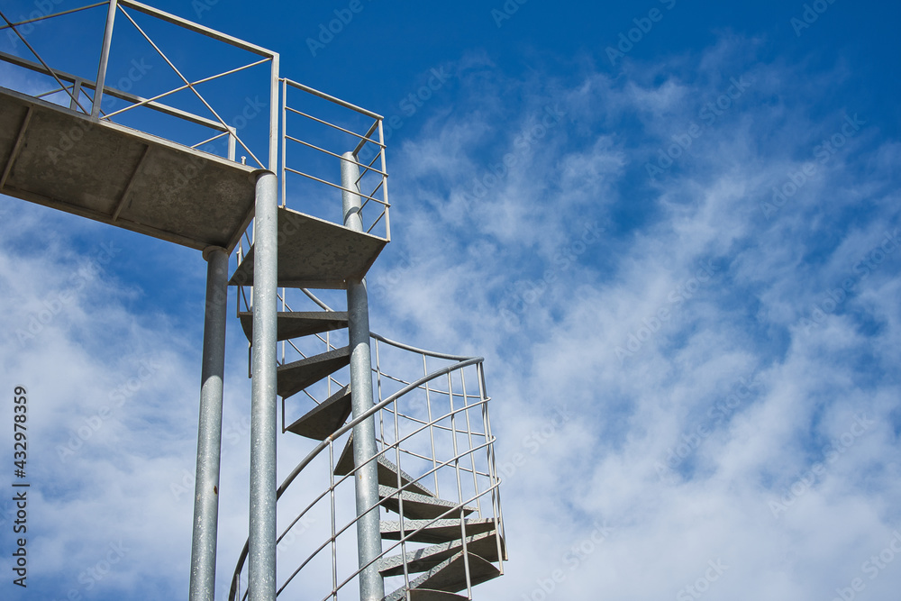Metal spiral staircase on a blue sky background. Copy space. Text Metal spiral staircase on a blue sky background. Copy space. Text