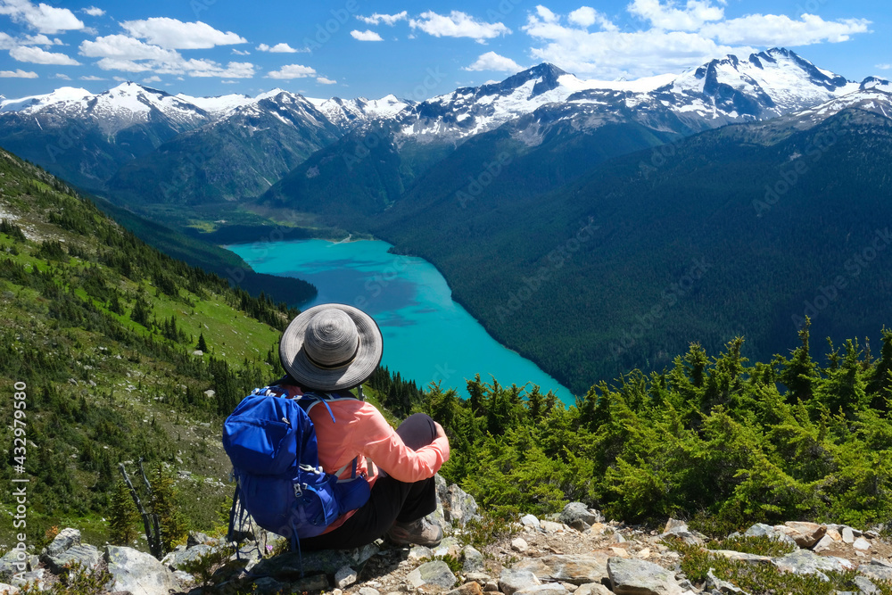 Woman backpacker on a high cliff above turquoise lake looking at view from High Note trail. Cheakamus Lake from Whistler Blackcomb mountain. British Columbia. Canada
