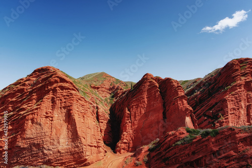Cliffs of seven bulls in the Jety-Oguz Canyon gorge  red rocks  erosion in clay  blue sky and steppe vegetation. Kyrgyzstan
