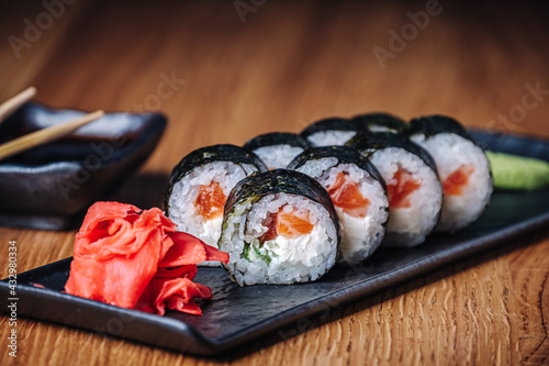Sushi on a wooden table in restaurant. Portion of sushi served on black plate with wasabi, soy sauce, ginger and chopsticks. Delicious Japanese food. Sliced tasty sushi rolls, close-up