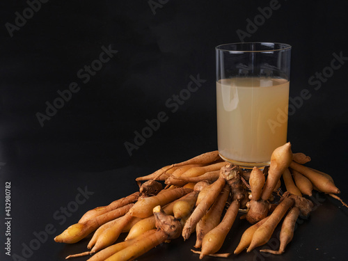 Finger root juice in transparent glass and fresh finger root on  black wooden  background Alternative herds for treating COVID-19.