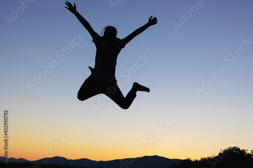 Silhouette of happy girl jumping playing on mountain at sunset