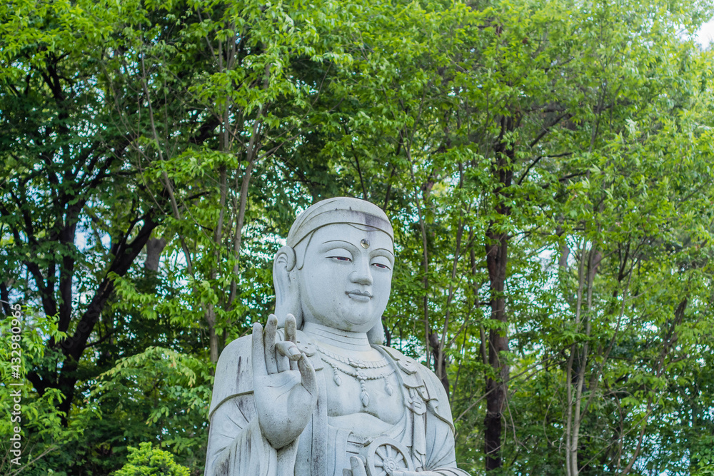 Closeup of large stone carved seated Buddha in front of lush green trees.