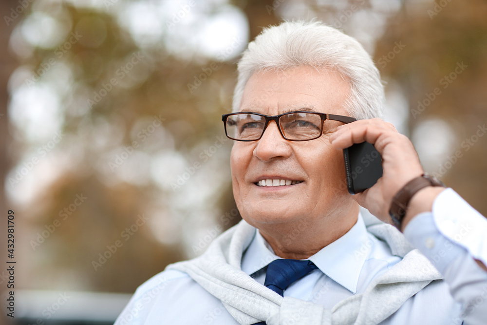 Senior businessman talking by mobile phone outdoors