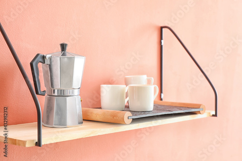 Shelf with coffee maker and cups hanging on color wall