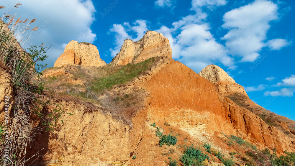 Landscape view clay cape cliffs. Green grass, lawns grown on slopes of clay mountains against blue sky. Hills of mountain and slopes of cape are overgrown with half grass and plants. Long web banner