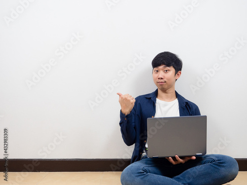 Handsome man sitting on the florr with laptop point finger at copy space confident face and happy smile white background photo