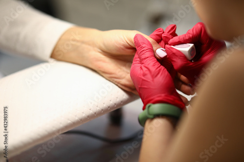 Close-up of woman using means of protection. Manicurist covering nails of client with light nail polish