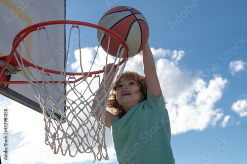 Kid basketball player making slam dunk in blue sky background. The child play sports.