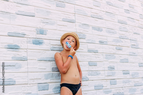Tanned boy in bathing trunks and hat eats ice cream