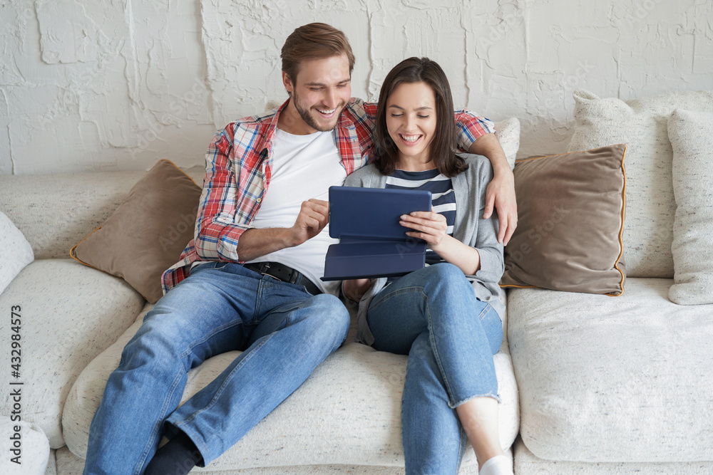 Young couple watching media content online in a tablet sitting on a sofa in the living room. Young couple watching media content online in a tablet sitting on a sofa in the living room.