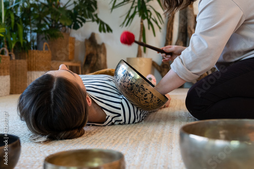 Obraz na plátně Tibetan singing bowls therapy for relaxation at home: young woman use sound massage for wellbeing, stress recovery and meditation
