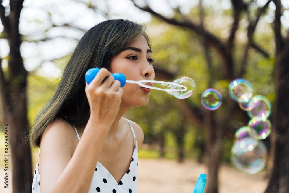 South East Asian ethnic 20s woman blowing air bubbles in the park Young Happy girl wears stylish dress with trees in background. Outdoor summer weekend activity - with copy space South East Asian ethnic 20s woman blowing air bubbles in the park Young Happy girl wears stylish dress with trees in background. Outdoor summer weekend activity - with copy space