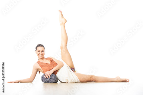 Young sporty healthy woman in bright white yoga studio, lying on bolster cushion, stretching, smilling, showing love and passion for bolster yoga.
