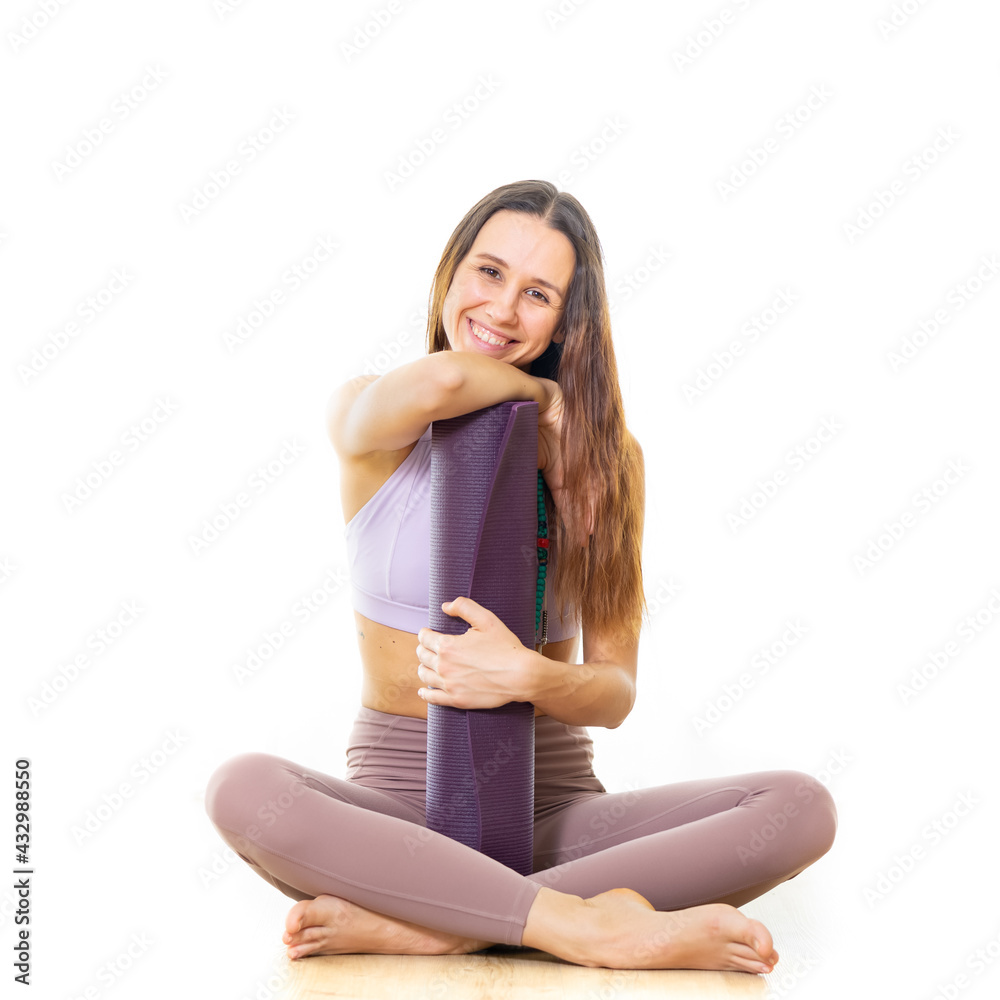 Young sporty female yoga instructor in bright white yoga studio, holding yoga mat, smiling, looking at camera Young sporty female yoga instructor in bright white yoga studio, holding yoga mat, smiling, looking at camera