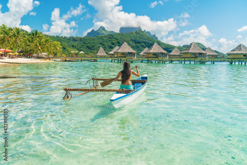 French Polynesia Tahiti travel vacation concept. Outrigger Canoe polynesian watersport sport woman paddling in traditional vaa boat. Water leisure activity, Bora Bora overwater bungalow resort hotel. photo