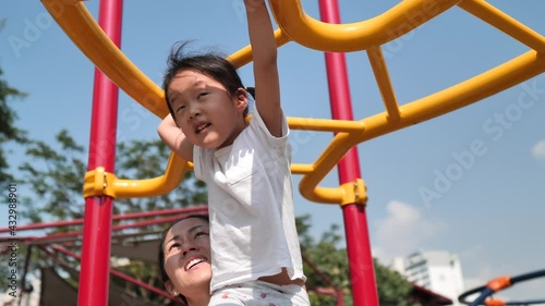 Asian chinese mum helping daughter across monkey bar swinging