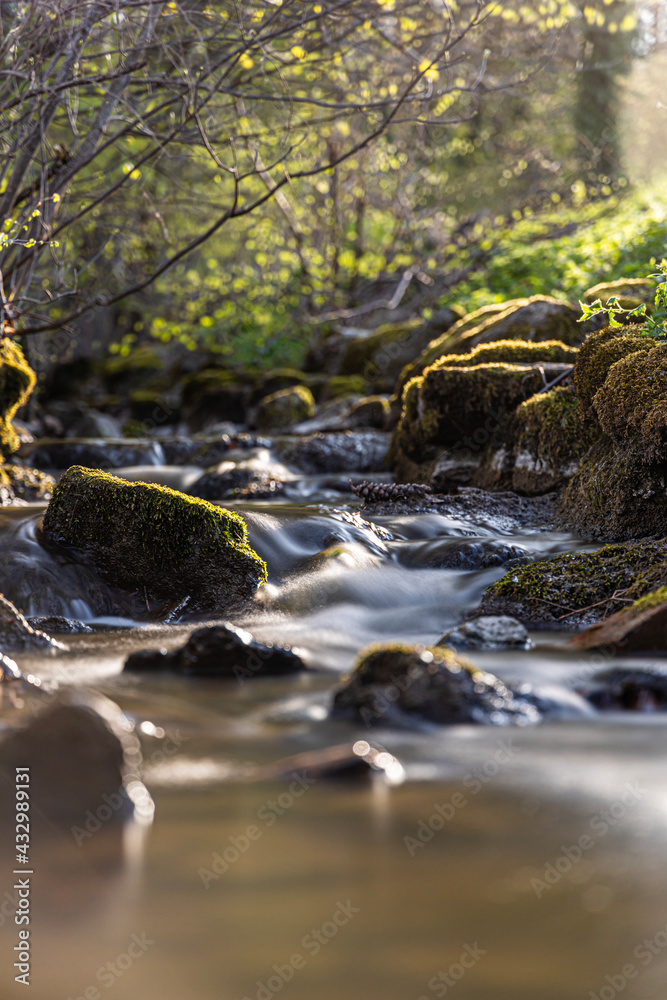 Fototapeta premium weicher Flussverlauf durch Moos bedeckte Steine im Frühling kurz vor Sonnenuntergang, Langzeitaufnahme