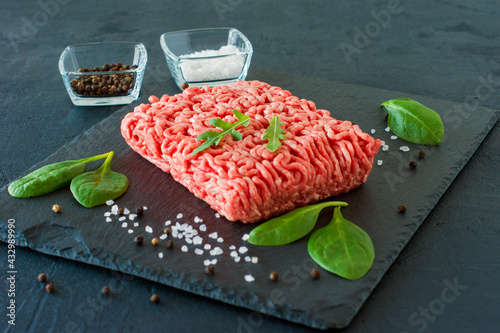 Raw minced beef meat on a slate with leaves and spices.